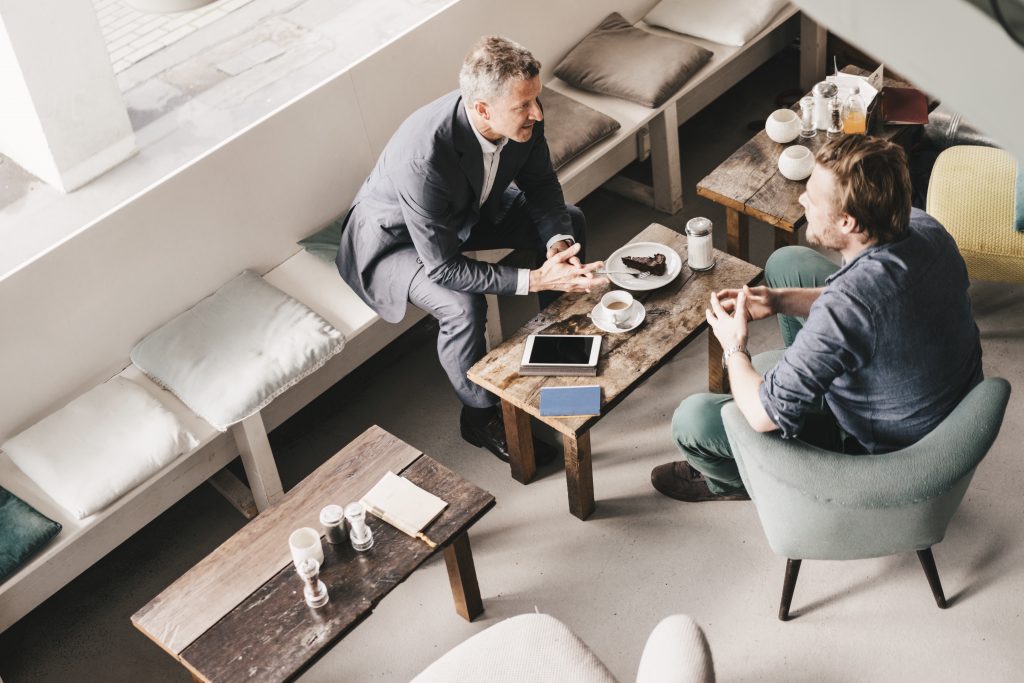 A man meets with his freelance designer in a coffee shop setting.