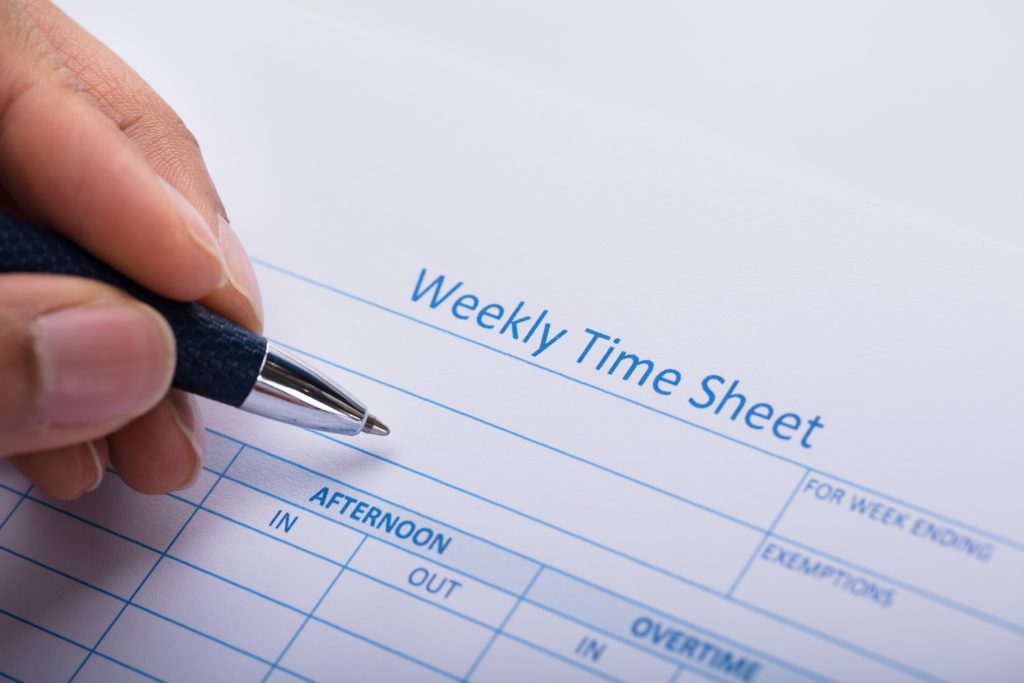 A hand fills out a weekly time sheet.